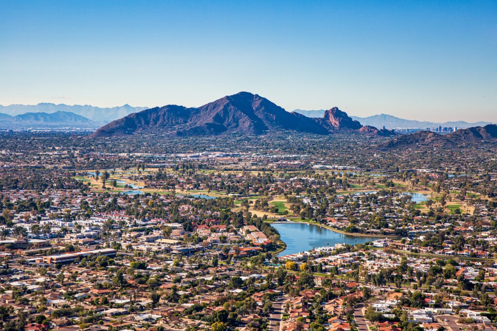 Aerial view of Scottsdale with a large lake, surrounded by houses, golf courses, and mountains.