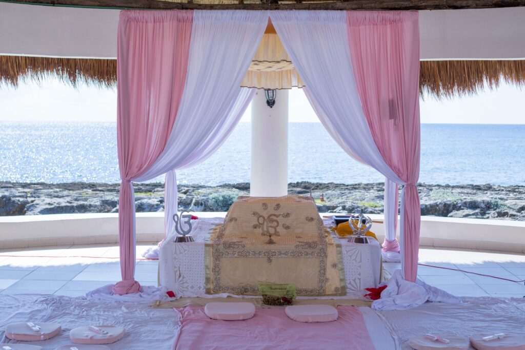 Akal Takht Bans Destination Weddings: A coastal Sikh wedding (Anand Karaj) setup, highlighting an adorned ceremonial space with pink and white drapes, set against a tranquil seascape