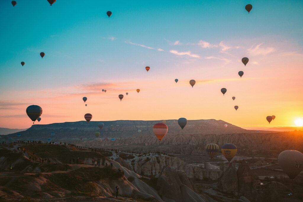 A serene sunrise scene with multiple hot air balloons floating above the rocky landscape of Cappadocia, Turkey.