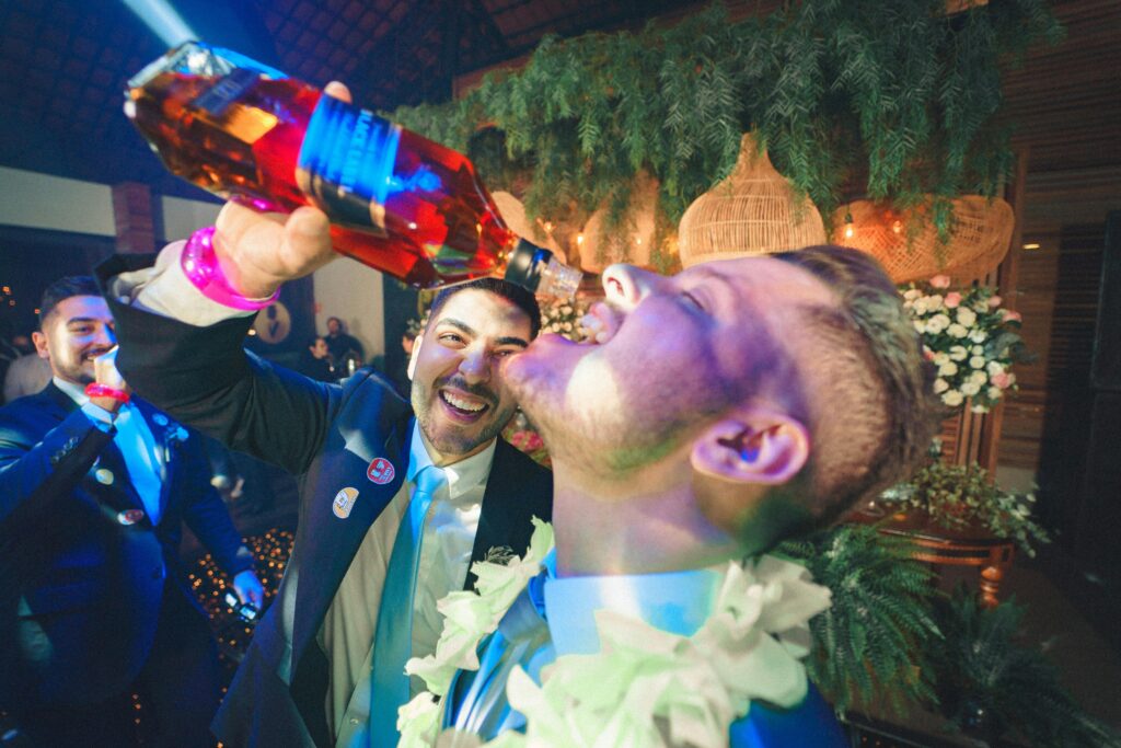 Groom and friend celebrating with a direct whiskey pour at a lively bachelor party