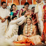 An Indian wedding ceremony with groom showering turmeric rice on the bride, surrounded by family.